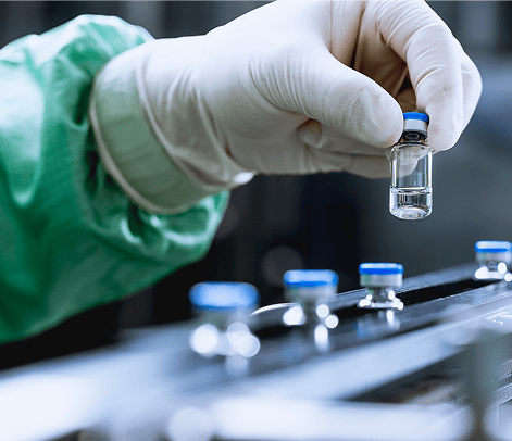 Gloved hand holding a small vial in a laboratory setting with more vials in the background.
