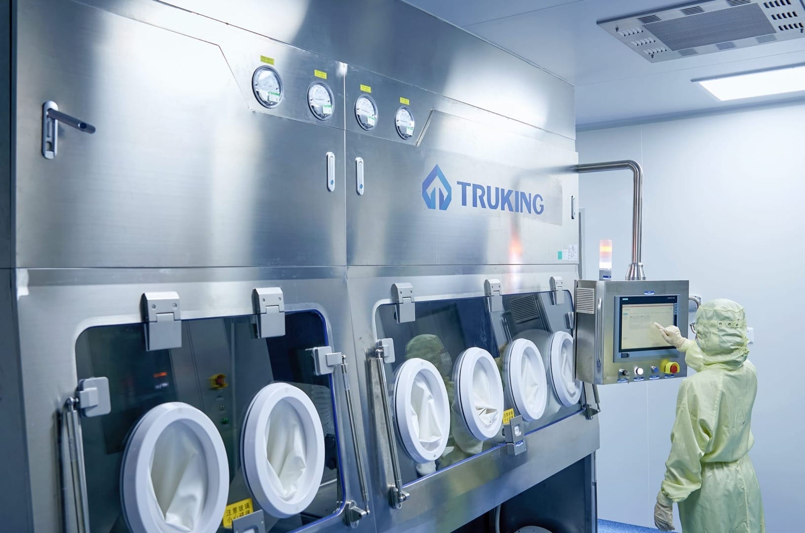 Worker operating pharmaceutical manufacturing equipment in a clean room environment with control panel and protective gear