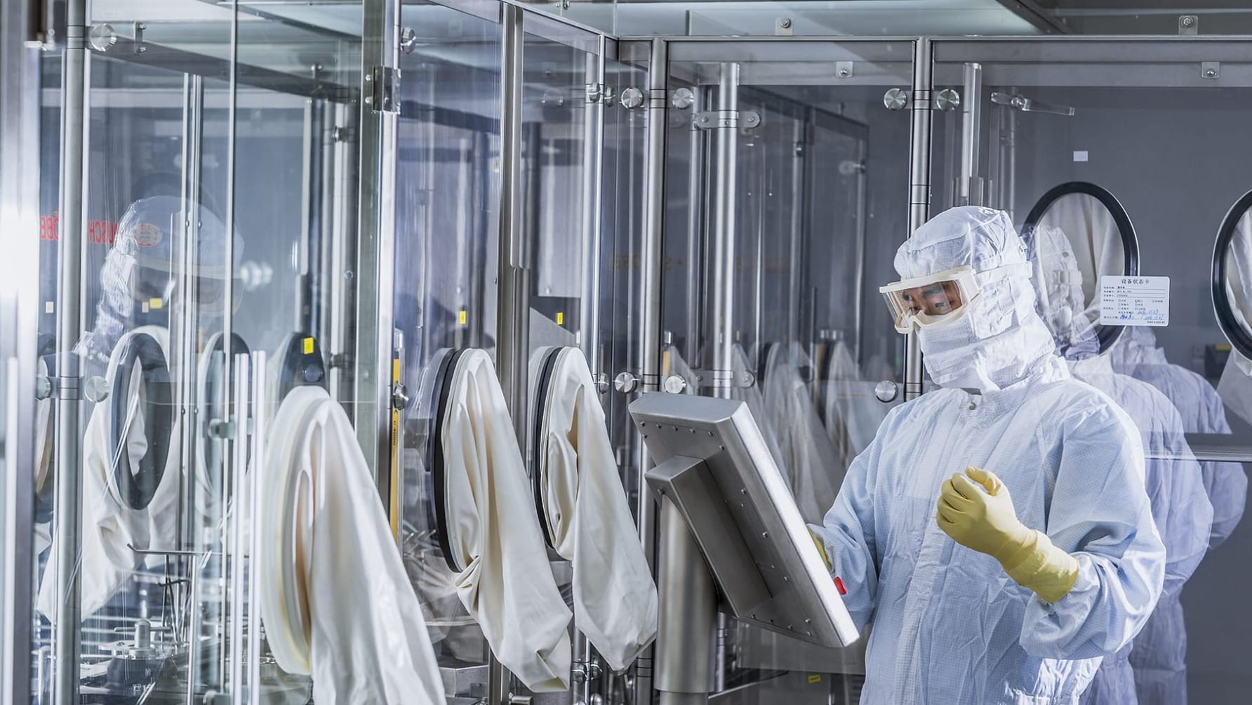 Scientist in protective gear operates equipment in a laboratory cleanroom environment.