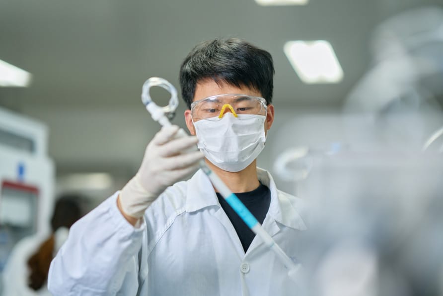 Scientist in protective gear examining lab equipment in a laboratory setting