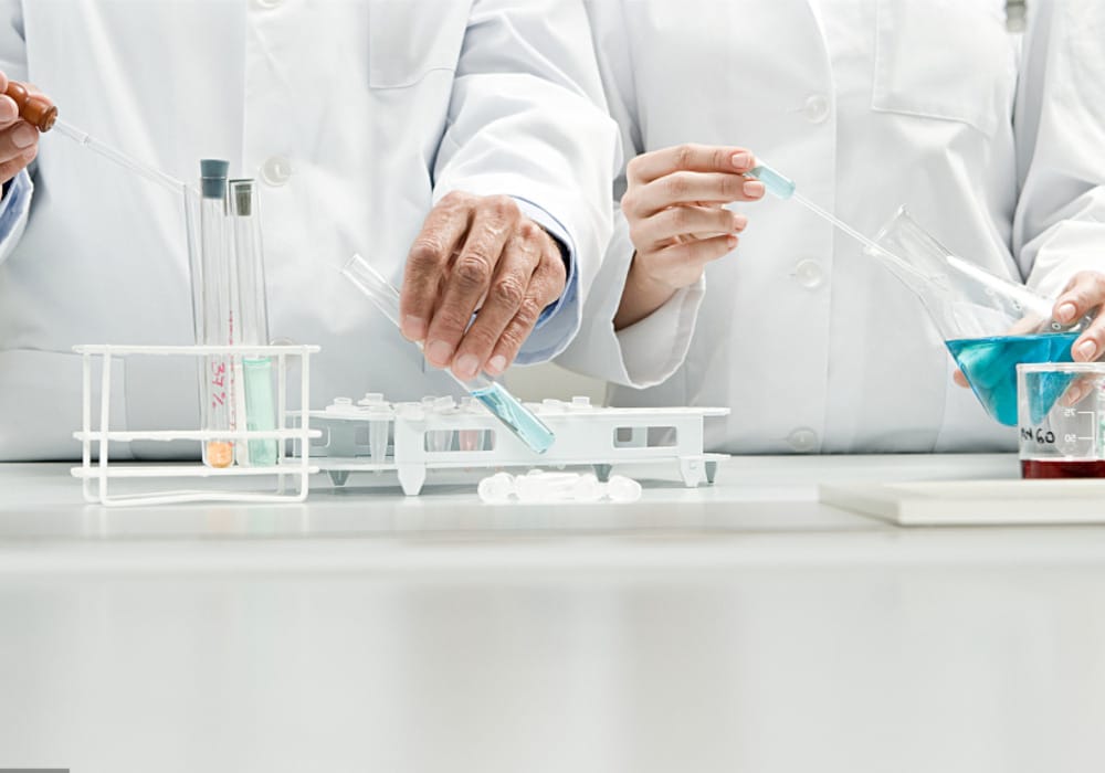 Scientists in lab coats conducting chemistry experiment with beakers and test tubes in a laboratory setting.