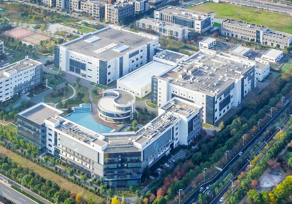 Aerial view of a large modern office complex surrounded by greenery and roads in an urban area.