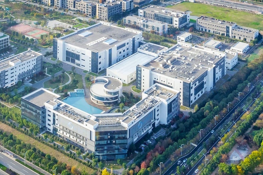 Aerial view of a large modern office complex surrounded by greenery and roads in an urban area.