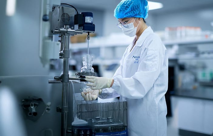 Scientist in a lab coat and mask conducting an experiment with lab equipment in a laboratory setting.